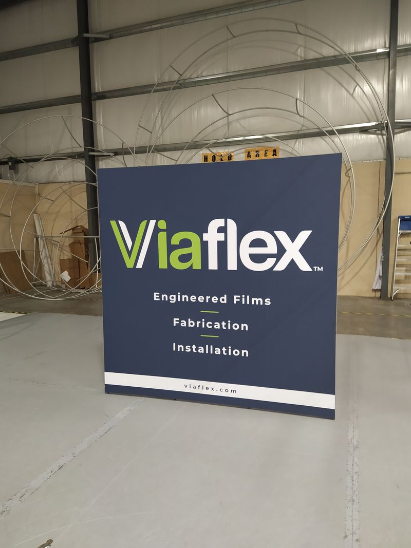 A close-up of a large gray display with "Viaflex, Engineered Films, Fabrication, Installation" printed on the front.