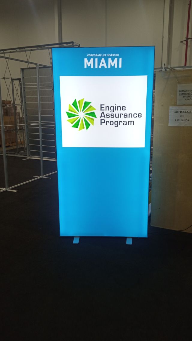 A close-up of a tall blue illuminated display with "Engine Assurance Program" printed on the front next to a green logo.
