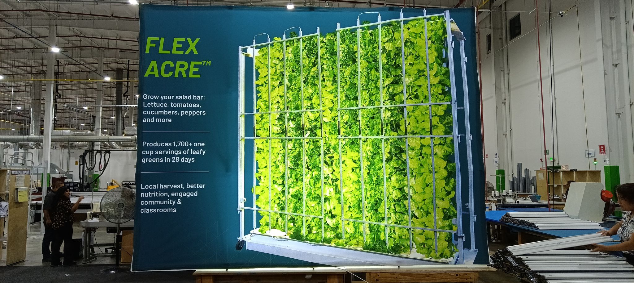 A Flex Acre display showing a vertical growing system filled with leafy greens inside a large workshop.