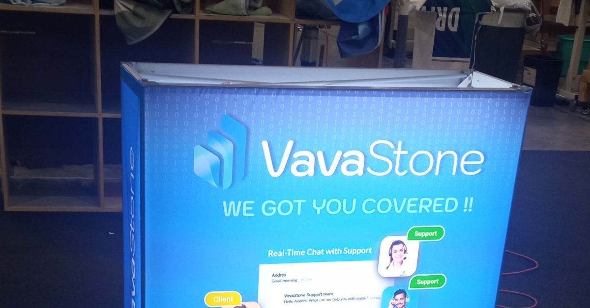A blue trade show display with VayaStone branding, a lit counter, shelves, and small items in front.